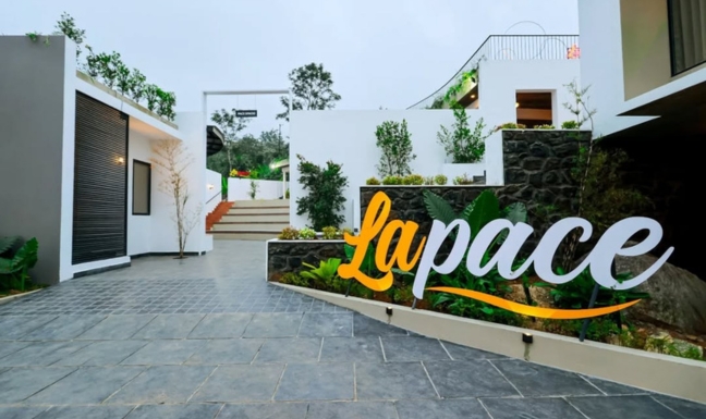 An elegant hilltop villa featuring traditional Kerala architecture blended with modern minimalism. The property is surrounded by morning mist and vibrant flower gardens.