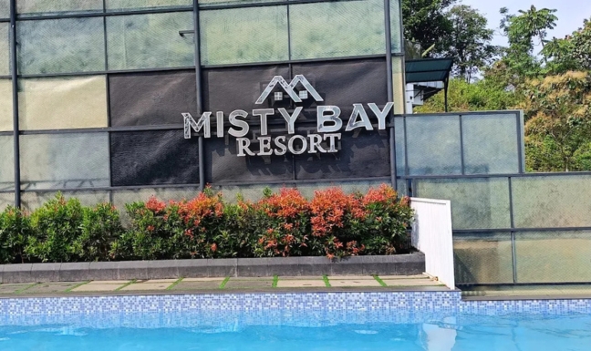 A luxurious infinity pool overlooking misty green mountains during a golden hour sunset. The architecture is modern and sleek with glass elements and lush landscaping.